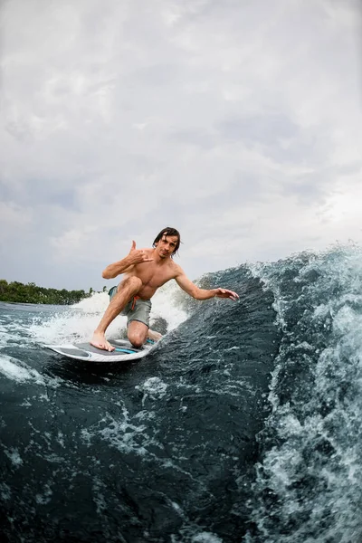 Homem ativo mostrar gesto mão montando a onda no wakeboard estilo surf — Fotografia de Stock
