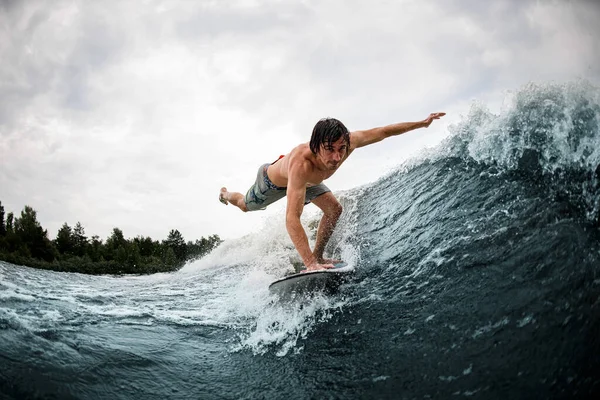 man make trick balancing on wake surf board on wave with stretching his leg and hand