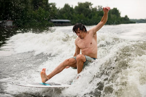 Aktiver nasser Mann versucht auf Waksurfbrett auf plätschernder Welle zu stehen — Stockfoto