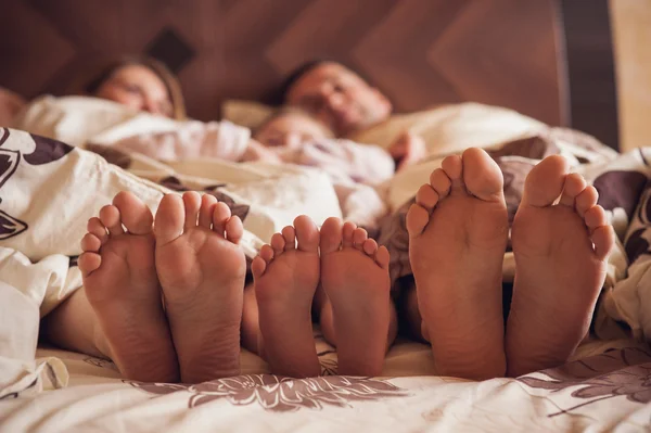 Famille sur le lit à la maison avec leurs pieds montrant — Photo