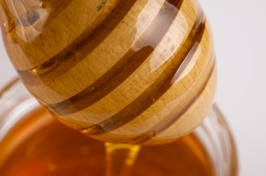 Glass can full of honey and wooden stick in it.  clipart