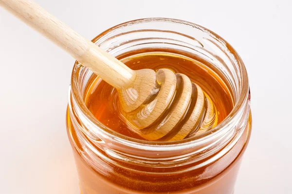 Lata de vidrio llena de miel y palo de madera . — Foto de Stock