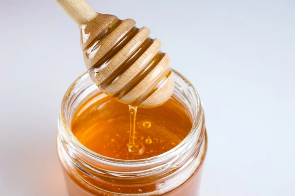Lata de vidrio llena de miel y palo de madera . — Foto de Stock