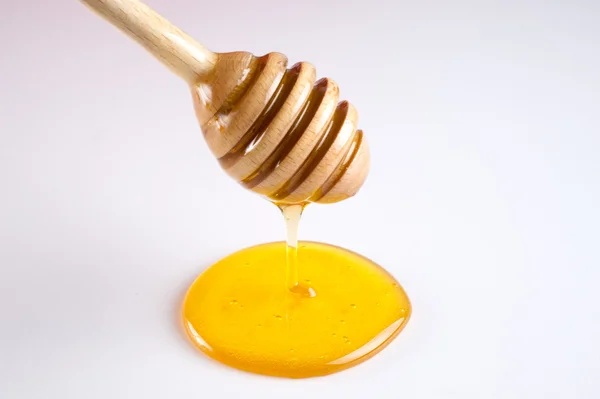 Miel goteando de una cacerola de madera aislada sobre el fondo blanco — Foto de Stock
