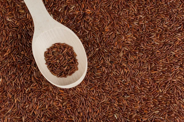 Arroz rojo en una cuchara de madera sobre fondo de arroz rojo . — Foto de Stock