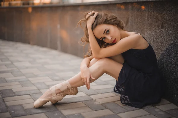 Balletdanser in zwarte jurk en pointe schoenen zittend op de grond — Stockfoto