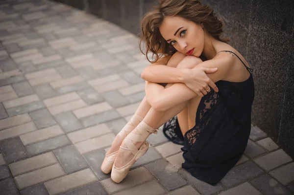 Ballet dancer in black dress and pointe shoes sitting on the ground — Stock Image Ballet dancer in black dress and pointe shoes sitting on the ground Stock Image