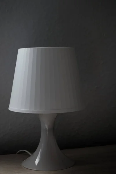 Vertical image of a white bedside lamp on a side-lit nightstand. Dark photography
