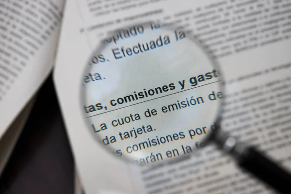 A magnifying glass points out on a paper the words in Spanish commissions, fees and expenses in a bank document