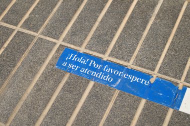 Yerde müşterilerin caddede anti-covid-19 önlemleri için beklediklerini gösteren bir tabela var. İspanyolca 'da 