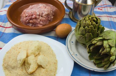 Et ile doldurulmuş enginarların hazırlandığı, zeytinyağı (EVOO), yumurta ve ekmek kırıntılarının doldurulmak için kullanıldığı bir masanın yakın çekimi