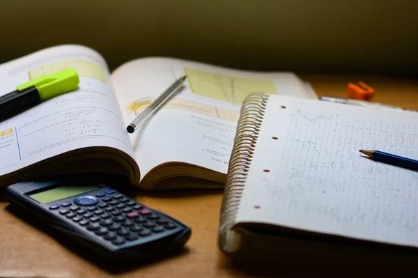 Table of someone who is studying mathematics, in which there is a book, an exercise book, a calculator and some writing instruments, such as a pen, a pencil and a highlighter pen
