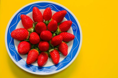 Yukarıdan bakıldığında, sarı bir masada taze çilek ve fotokopi alanı olan bir tabağın yakın çekimi