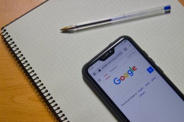 Google sayfası açık bir mobil gördüğümüz düz masa, bir not defteri ve bir kalem.