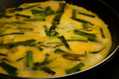 Close up of a chopped garlic omelette with the egg without curdling in a frying pan on a black glass ceramic hob