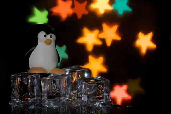 Özgür yazılımın penguen amblemi, Tux, arka planda çok renkli yıldızlar olan buz küpleri üzerinde