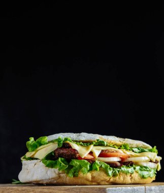 Arka planda sokak yemekleri ve fast food üzerine pembe içecek kokteyli olan büyük bir sandviç. Biftekli ev yapımı hamburgerler, ahşap masada peynir. Tonu ayarlanmış resim.