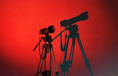 Üç ayaklı kamera, duvardaki kamera gölgesi, kırmızı arka plan.