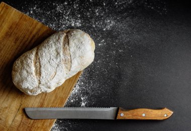 Masadaki siyah arkaplan ununda bıçaklı ekmek.