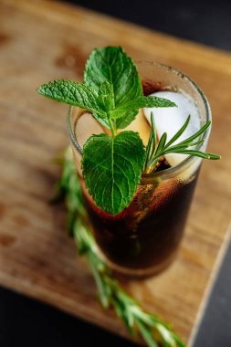 Siyah zemin üzerinde buz, nane ve biberiye ile bir bardak kola.