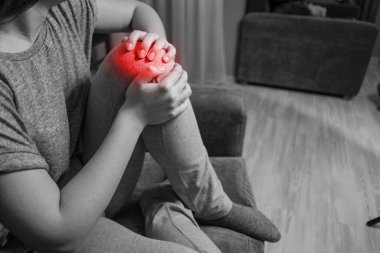 Genç kadının diz ağrısı var, siyah beyaz fotoğraf kırmızı aksan, acıya yakın.