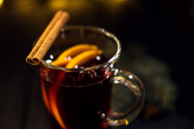 Tarçın bir bardakta, portakal ve tarçınlı sıcak şaraba yakın, koyu siyah arka planda, Noel ağacı ve ışıkları, büyük sarı bokeh, sıcak şarap seti