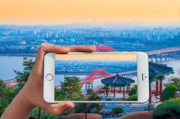Mão segurando telefone inteligente tirar uma foto na ponte Banghwa . — Fotografia de Stock