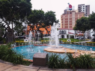 Centroamerica Parkı 'nda büyük ağaçlar, bitkiler, çiçekler, arka plandaki evler, hareket halindeki arabalar ve şehir çevresi Miraflores Lima Peru ile çeşme