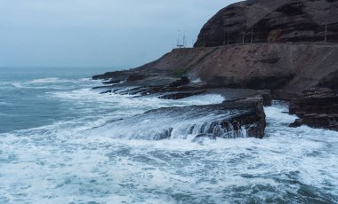 Chorrillos Lima Peru 'daki sahil şeridi, bulutlu bir günde La Herradura sahilindeki kayalara çarpan dalgalar.