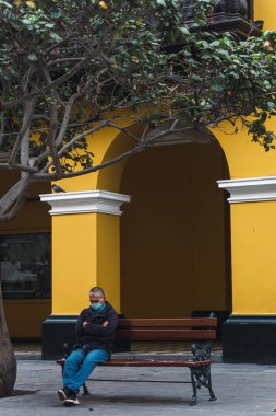 Lima 'nın tarihi merkezinde Santa Rosa geçidi, koloni sarı binalarının yolu, salgın zamanlarında ameliyat maskesiyle bankta uyuyan yaşlı bir adam, eski bir ağaç.