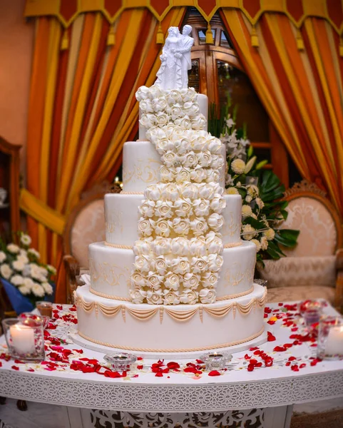 赤いバラで飾られた白いテーブルの上にウェディングケーキ ケーキの上に結婚式の彫像 — ストック写真