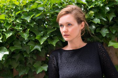 Yeşil yaprakları ile ahşap bir çit önünde duran orta yaşlı kadın.