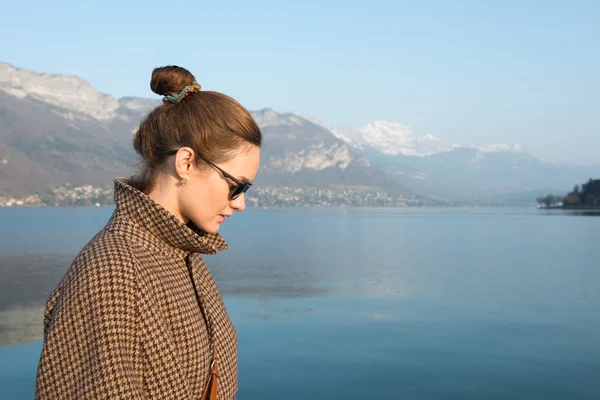 Hermosa mujer en gafas de sol sobre un fondo de lago y montañas . — Foto de Stock