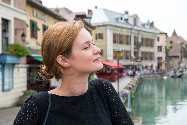 En ung kvinna är ständiga och leende. I bakgrunden, franska gatan och kanalen. — Stockfoto