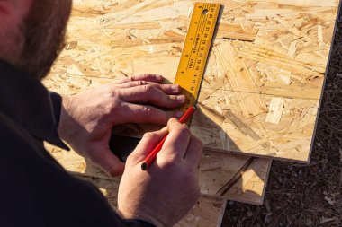 İşçi bir kare ve bir kalem kullanarak OSB sayfasında ölçümler ve işaretler alır