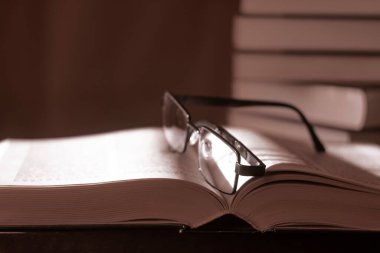 Sayfalarda gözlük ve arka planda bir yığın kitap olan açık bir kitap. Seçici yumuşak odaklanma. Tonlama. Kopyalama alanı.
