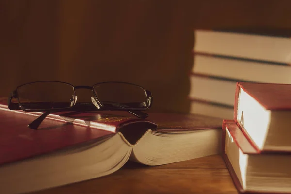 Glasses on an overturned open book against the background of stacks of books. Selective soft focus.