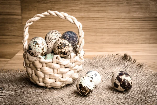 Quail eggs in a basket on a wooden background — Stock Photo, Image