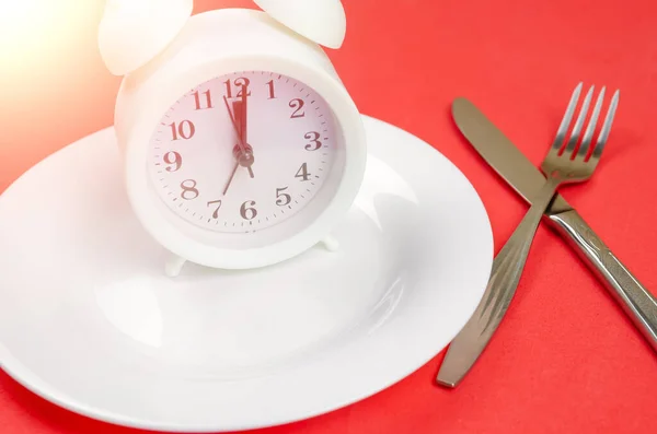 白色闹钟坐在一个白色的盘子上 红色的背景 叉子和刀关闭 晚餐的概念时间 — 图库照片
