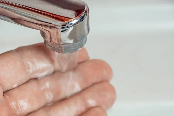 Close-up of a man\'s hand under a stream of clean water from a tap, copy space