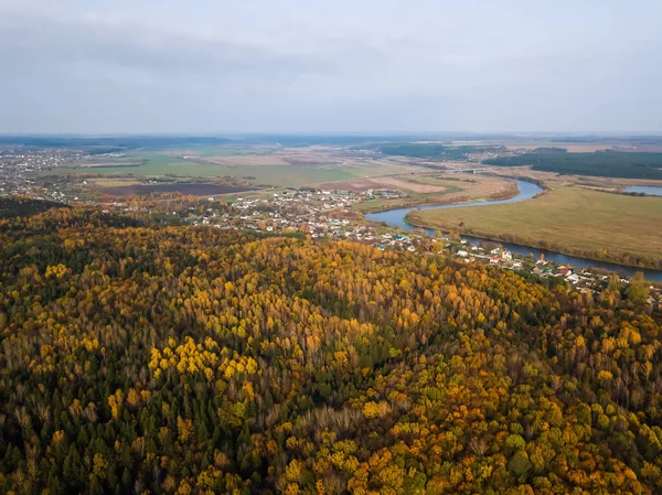 Drone view of a beautiful autumn forest, village, river on a Sunny day. Beautiful autumn landscape with river and countryside.