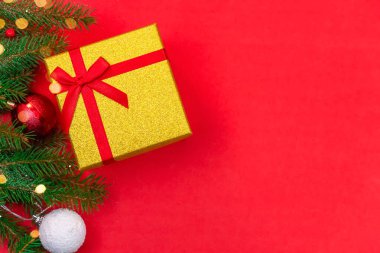 Kırmızı fiyonklu hediye kutusu, ladin dalı ve karlı Noel topları ve kırmızı arka planda fotokopi alanı ile yakın plan, üst manzara. Noel veya Yeni Yıl arkaplanı.