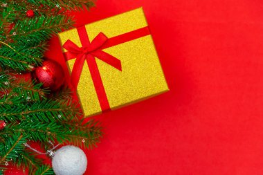 Kırmızı fiyonklu hediye kutusu, ladin dalı ve karlı Noel topları ve kırmızı arka planda fotokopi alanı ile yakın plan, üst manzara. Noel veya Yeni Yıl arkaplanı.