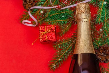 Şampanya şişesi, kırmızı hediye kutusu, Noel ağacı dalı, kar, kırmızı arka planda fotokopi alanı, üst manzara. Güzel Noel arkaplanı