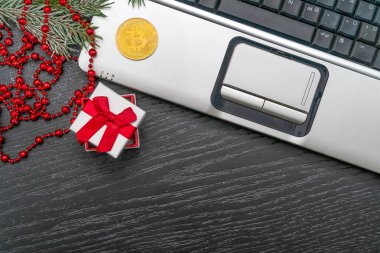 Bitcoin, kırmızı boncuklar, noel ağacı dalları, fotokopi alanı olan hediye kutusu, üst görünümü olan karanlık bir masada kompozisyon dizüstü bilgisayarı. Kripto para birimi. Noel hediyesi, yeni yıl.