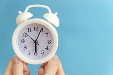 Kadınların elleri, üzerinde kopya alanı olan mavi bir zemin üzerinde beyaz bir çalar saat tutuyor.