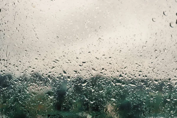 Pencere camında yağmur damlaları ve arka planda ağaçlar. Yağmurlu hava, arka plan