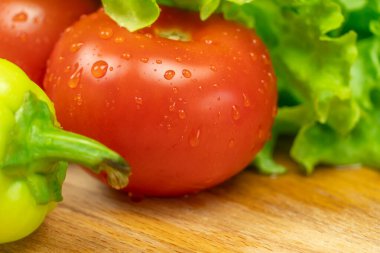 Su damlalı güzel, sulu sebzeler Biberler, domatesler, ahşap bir tahta üzerinde marul yaprakları