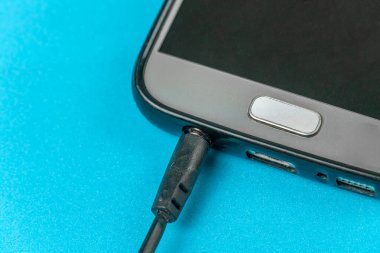 Sarı arka planda cep telefonunun yanındaki deliğin yanındaki siyah kulaklığın fişi, makro fotoğraf.