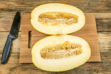 Tahtada ortadan ikiye bölünmüş sarı kavun, bir bıçağın yanında.